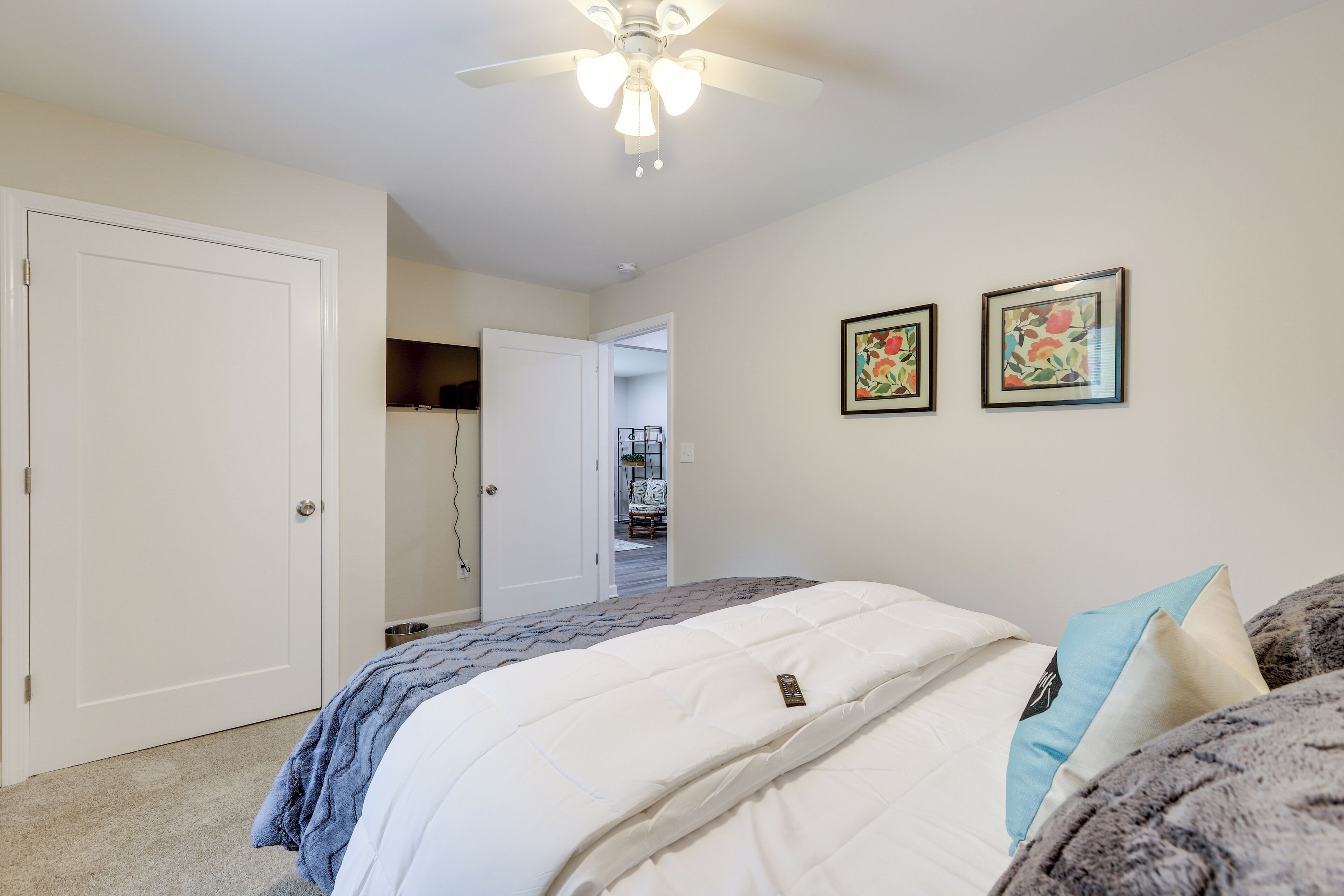A bedroom with a bed, a ceiling fan, and two framed pictures on the wall.