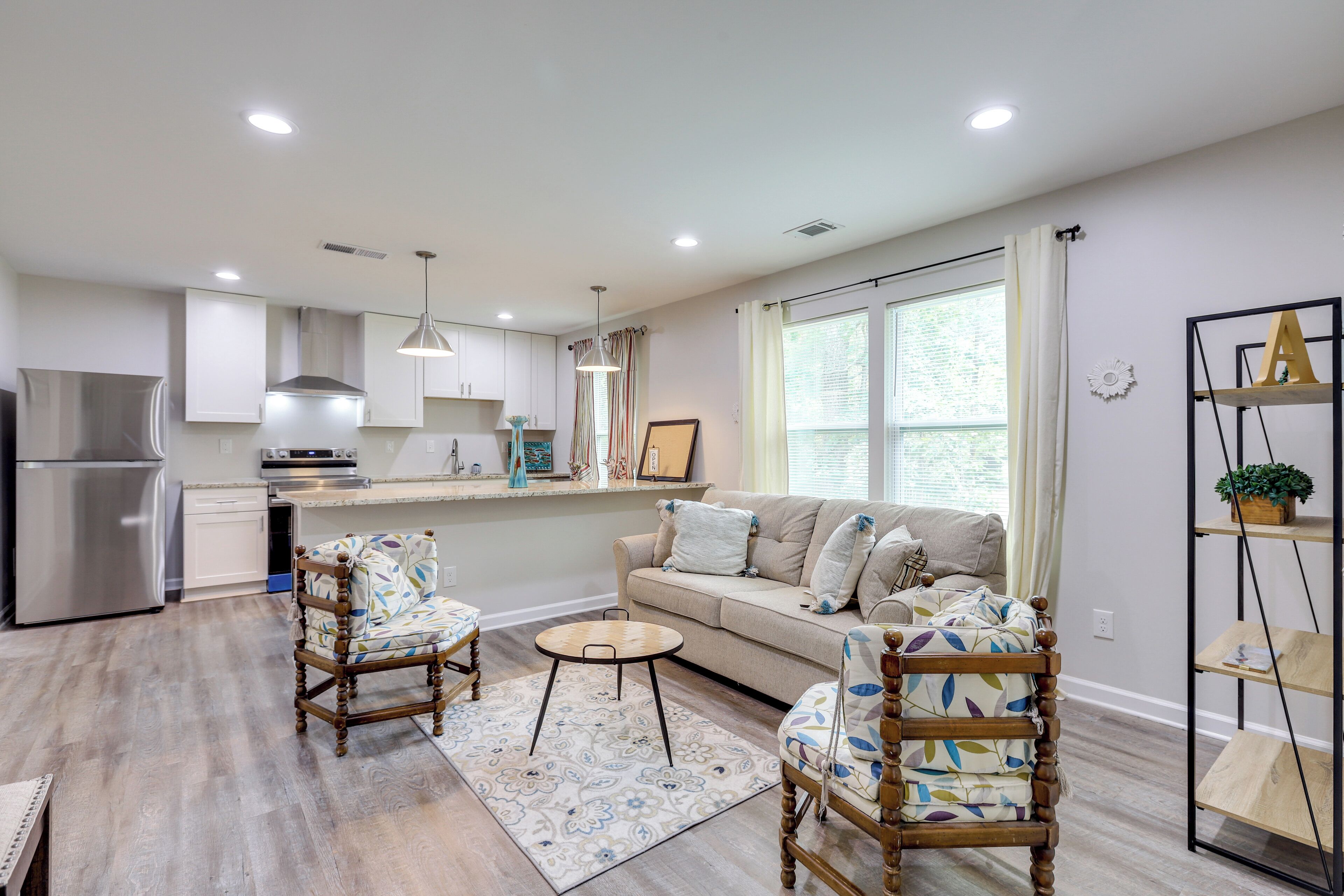 A modern kitchen with built-in appliances, a dining area with a round table, and a living room with a sofa and two chairs.