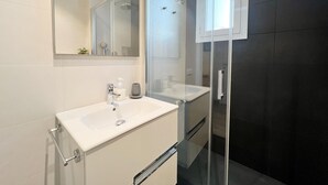 Ett modernt badrum med ett vitt handfat, en duschkabin i glas och en stor spegel.