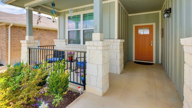 A covered porch with a brick wall, a wooden door, and a small garden area with potted plants. - Remote Working Hub w/ Yard in South Austin Suburbs (Kyle)