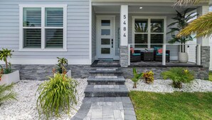 A modern house with a grey exterior, a stone pathway leading to the front door, and a number '5484' on the post.