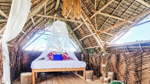 A thatched-roof bedroom with a bed, wooden floor, and woven mats. - Honeymoon Nest Zanzibar in Jambiani (Jambiani)