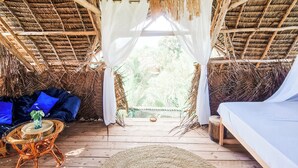A thatched-roof room with a bed, a wicker table, and a hanging basket. - Honeymoon Nest Zanzibar in Jambiani (Jambiani)