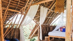 A cozy, rustic room with a thatched roof, a bed with a canopy, a wicker chair, a glass table, and a woven rug. - Honeymoon Nest Zanzibar in Jambiani (Jambiani)