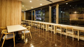 A restaurant with a long wooden table and chairs, large windows, and a wooden floor. - HOTEL AMANEK Asakusa Sakurabashi (Tokyo)