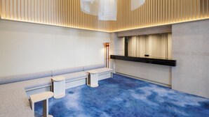 A modern reception area with a blue carpet, a bench, and a reception desk. - HOTEL AMANEK Asakusa Sakurabashi (Tokyo)