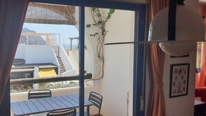 A balcony with a table and chairs, a view of the sea, and a plant on the wall.