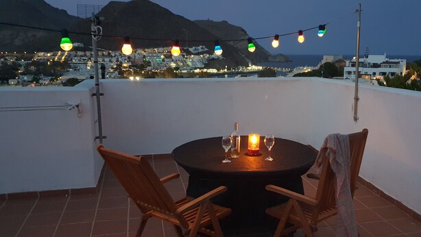 A terrace with a round table, two chairs, a candle, and string lights.