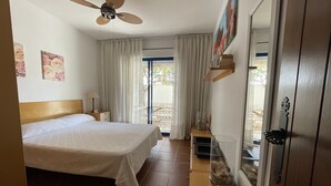 A bedroom with a bed, a ceiling fan, a nightstand, a lamp, a glass fish tank, and a door with a handle.