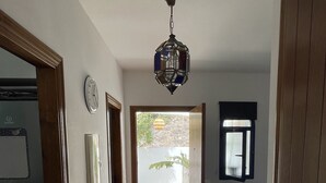 A hallway with a tiled floor, a clock, a door with a window, and a hanging light fixture.