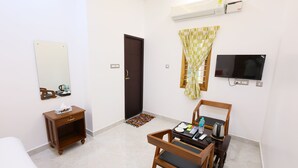 A hotel room with a bed, a wooden nightstand, a TV, a small table with a tray, and a window with a checkered curtain. - Star Eden Residency (Chinna Veerampattinam)