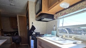 Cucina compatta per camper con mobili in legno, un fornello e una finestra che si affaccia su un parcheggio.