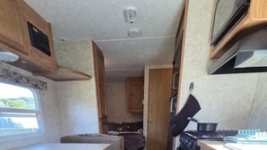 Una cucina compatta per camper con fornello, microonde e un piccolo angolo ristoro.
