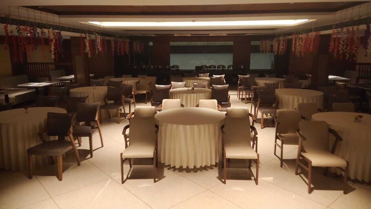 Un salón de conferencias con mesas y sillas redondas, una pantalla grande al frente y adornos florales en las paredes.