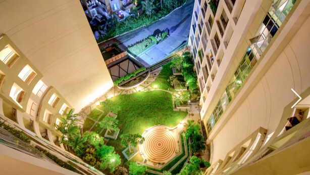 Un edificio de gran altura con un patio central que presenta una fuente circular, rodeado de follaje y senderos.