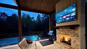 A modern outdoor living area with a stone fireplace, a comfortable sofa, and a large flat-screen TV mounted on a wall.