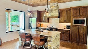 A modern kitchen with a large island, wooden cabinets, and a stone accent wall.
