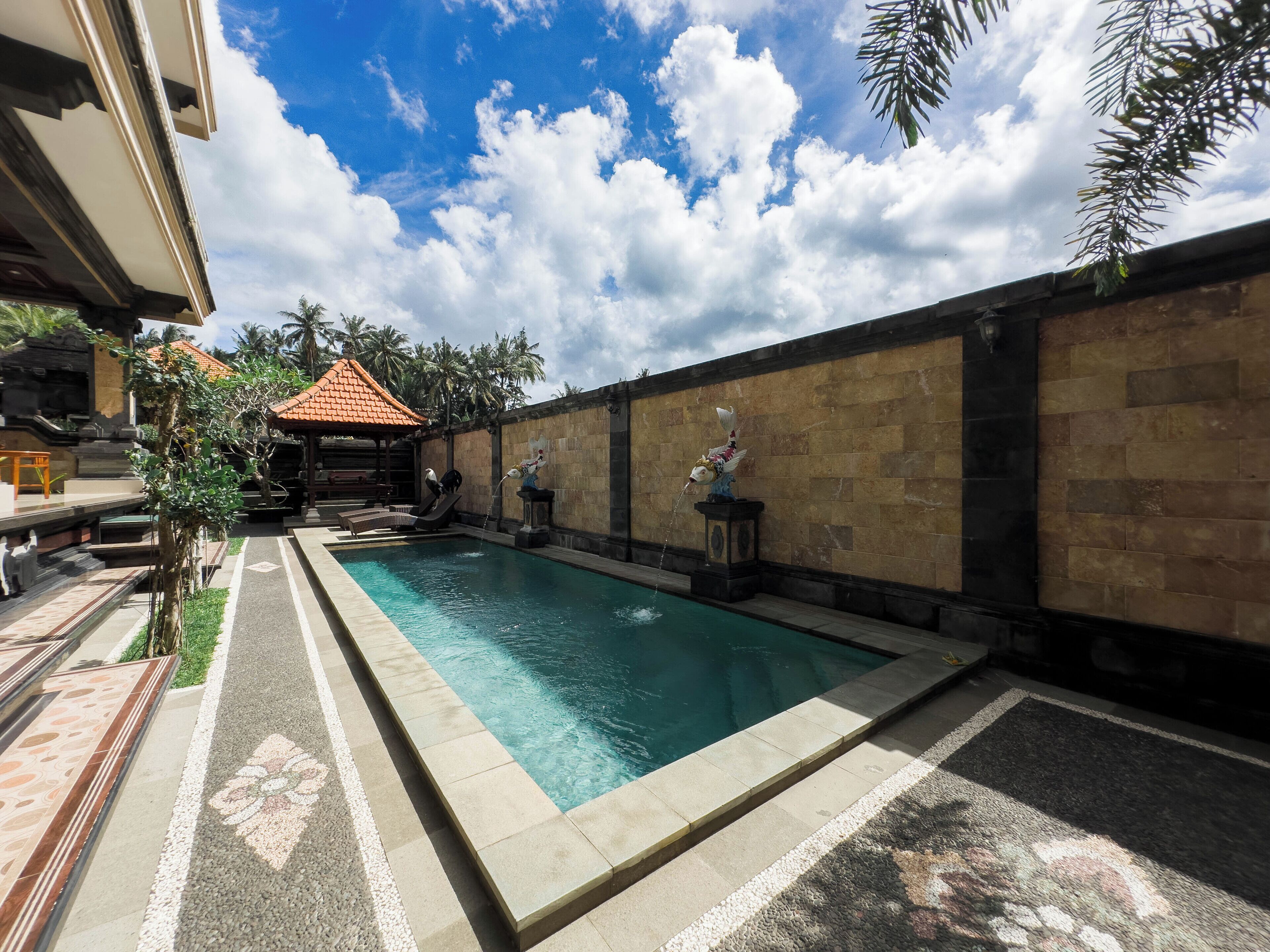 A swimming pool with a tiled deck, a stone wall, and a small pavilion with a tiled roof.