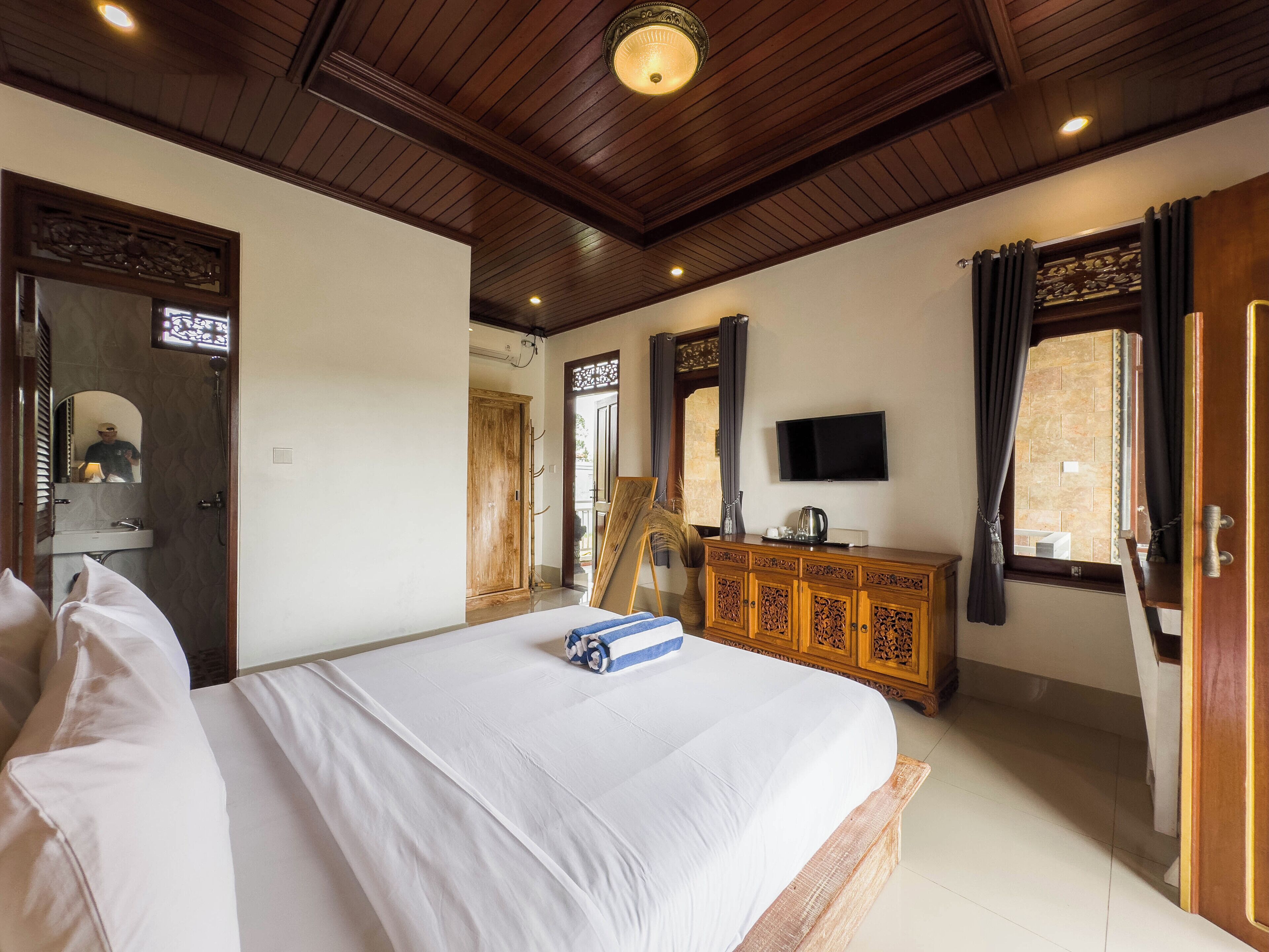Un dormitorio con una cama grande, techo de madera, televisión en la pared y un armario de madera.