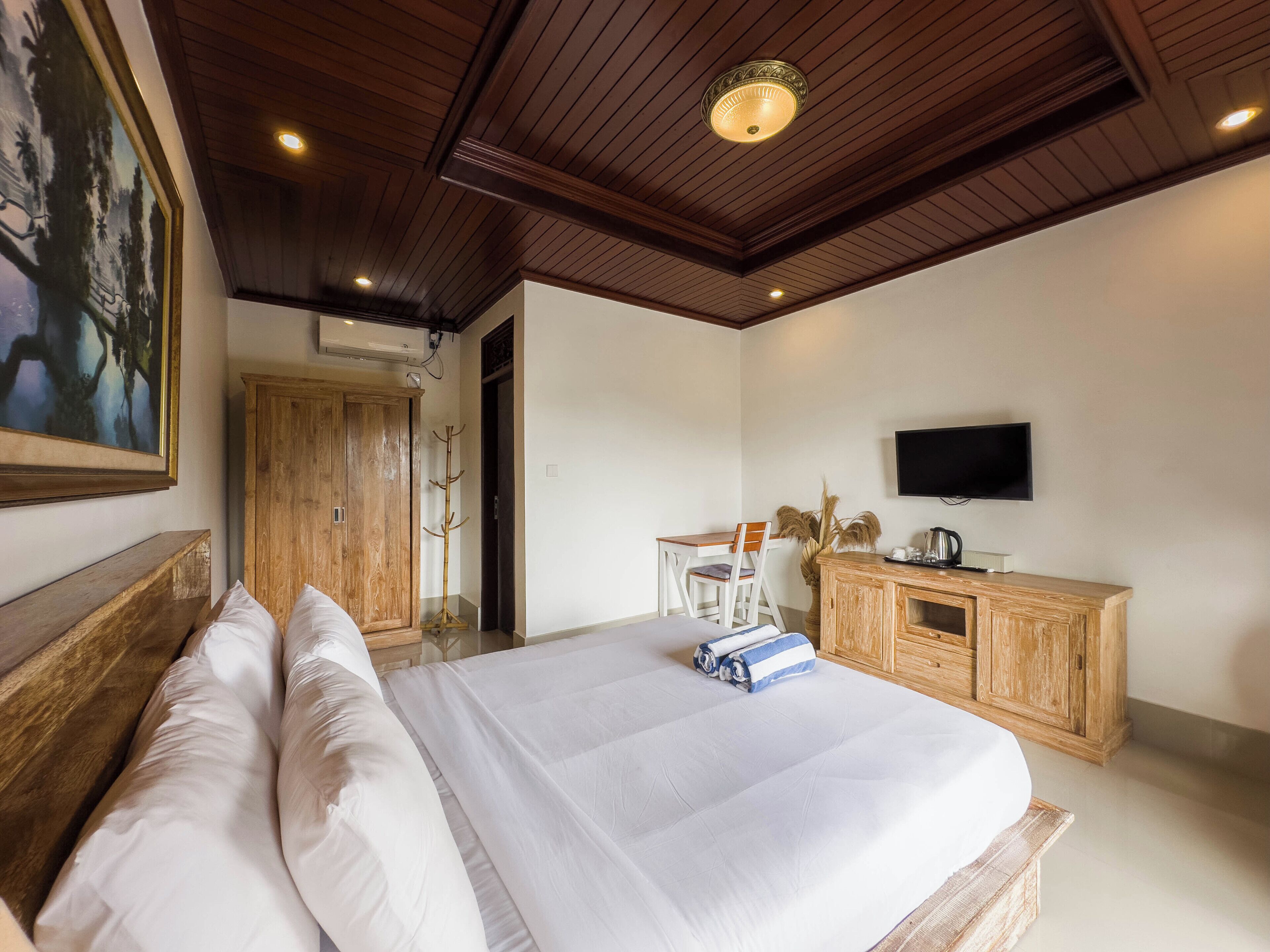Une chambre à coucher avec un grand lit, une tête de lit en bois, un téléviseur fixé au mur et une armoire en bois.