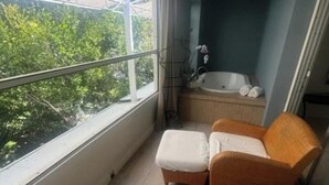 A balcony with wicker furniture, a bathtub, and a view of greenery. - Jacuzzi Retreat W/ Garden View @Islamorada - Wild Water Suite (Islamorada)