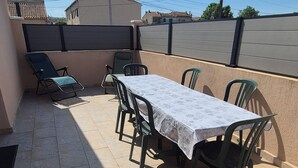 An outdoor patio with a table and chairs, a covered seating area, and a view of the street and buildings in the background. - Top of villa in charming Provencal village (La Crau)
