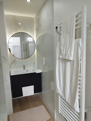 A modern bathroom with a marble vanity, a round mirror, a towel rack, and a shower area. - Aurore's cottage (Pernant)