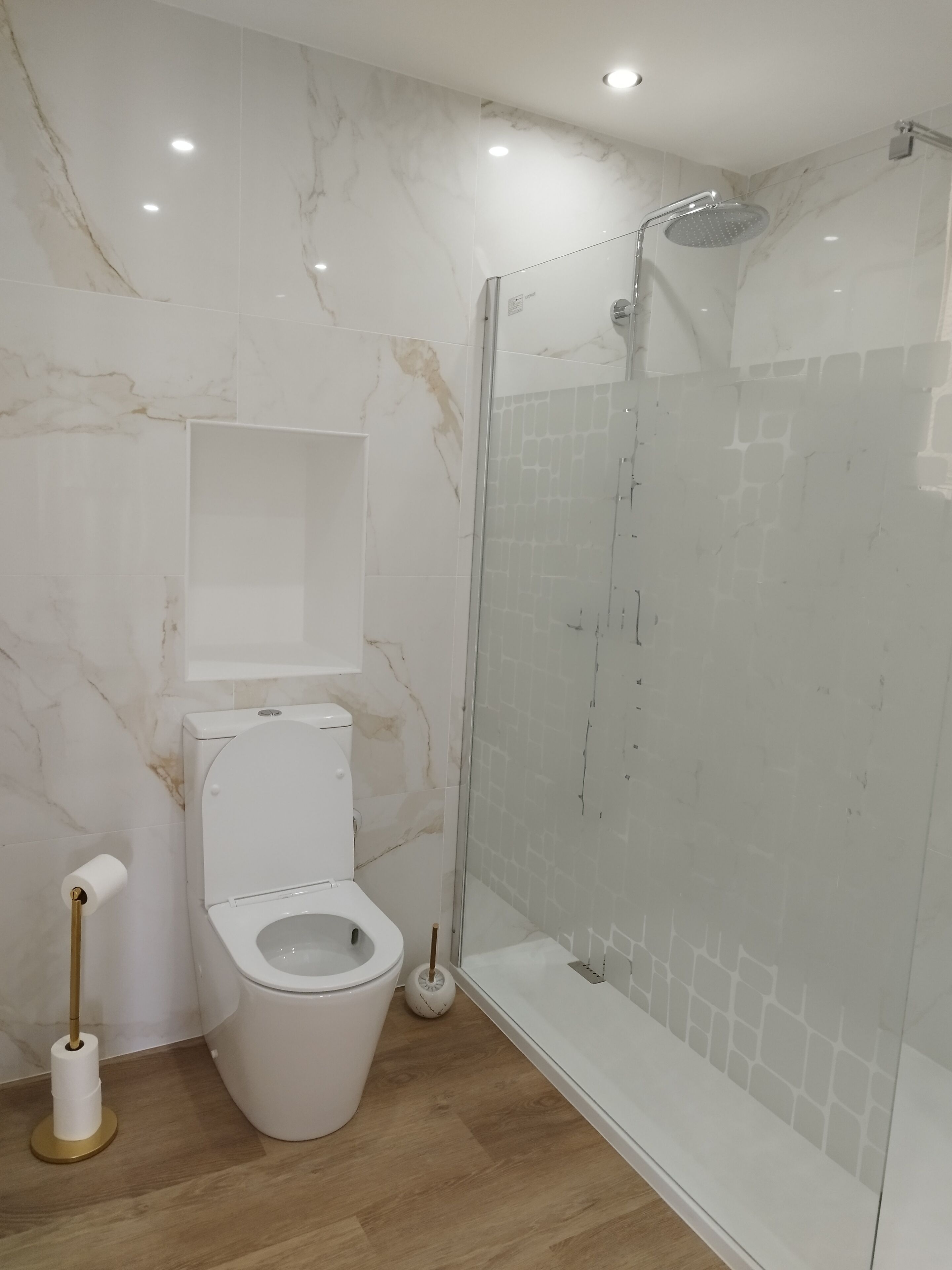 A modern bathroom with a toilet, a shower enclosure, and marble walls.