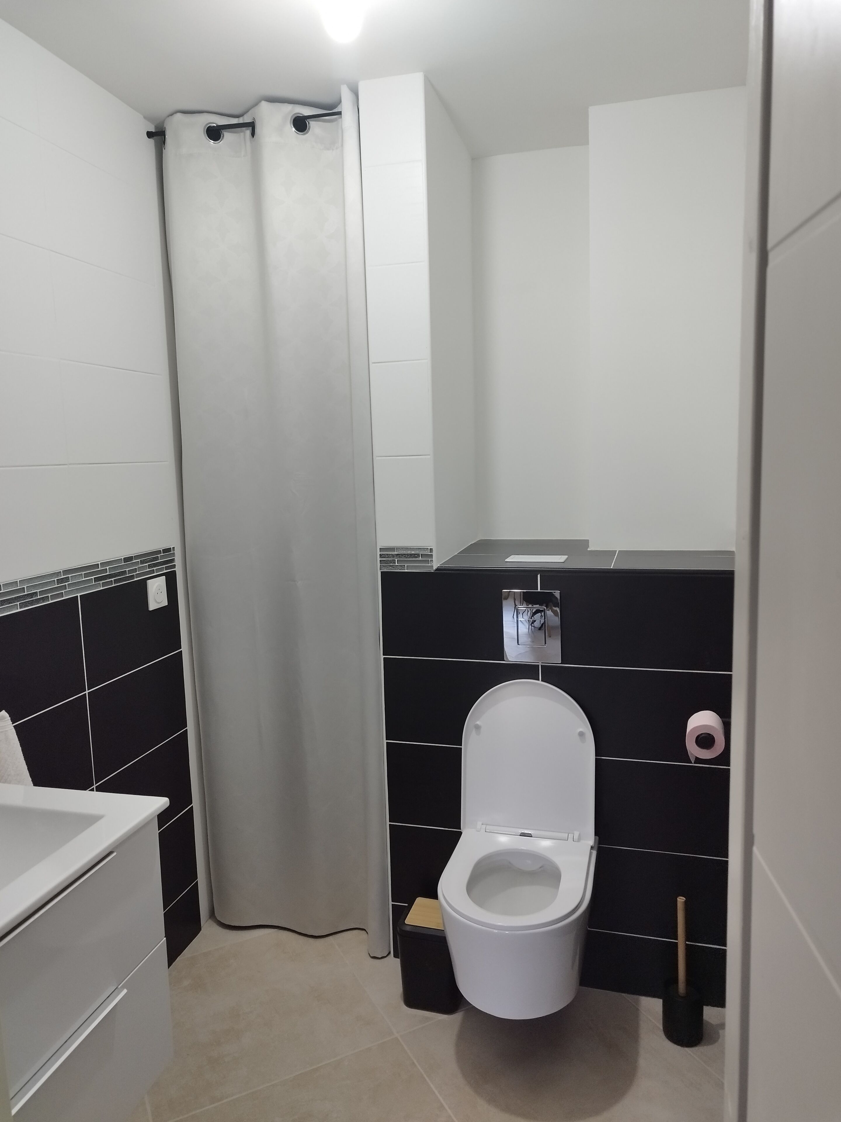 Un baño moderno con inodoro blanco, paredes con azulejos negros y cortina de ducha.