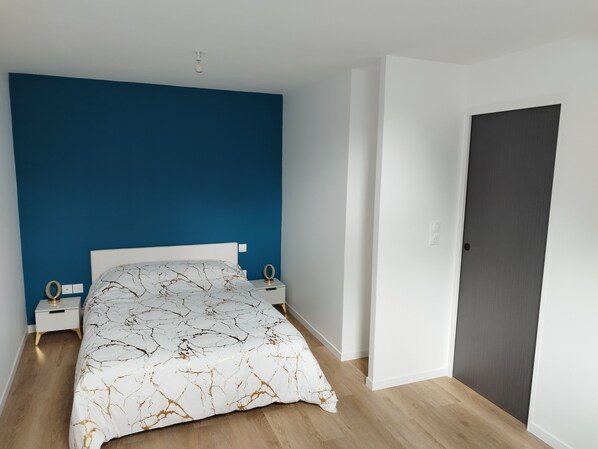 A bedroom with a bed, a nightstand, a door, and a blue wall. - Aurore's cottage (Pernant)