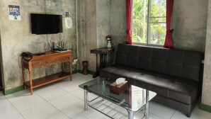 A living room with a sofa, a glass coffee table, a TV, a wooden console table, and a fan. - Phanumas LongStay Resort  (San Pa Thong)