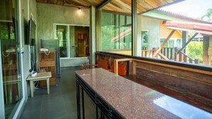 A modern kitchen with a granite countertop, wooden ceiling, and large windows offering a view of outdoor structures. - Phanumas LongStay Resort  (San Pa Thong)