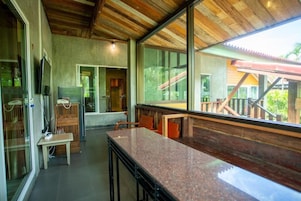Uma cozinha moderna com bancada de granito, teto de madeira e grandes janelas com vista para construções externas.