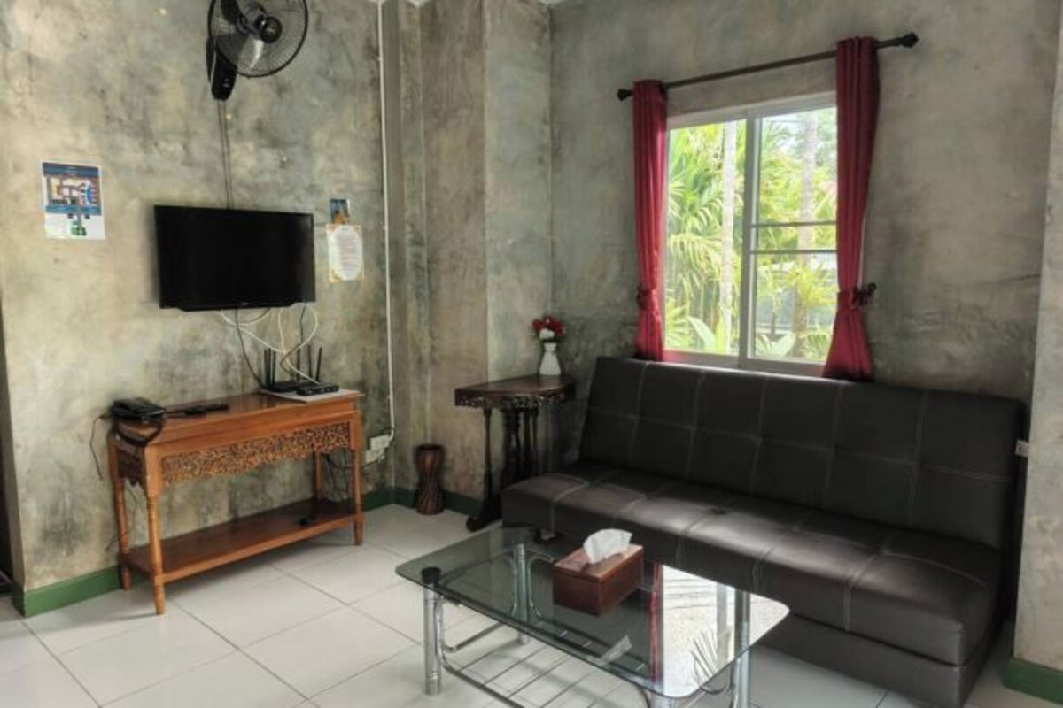 A living room with a sofa, a glass coffee table, a wooden console table, a television, and a window with curtains.