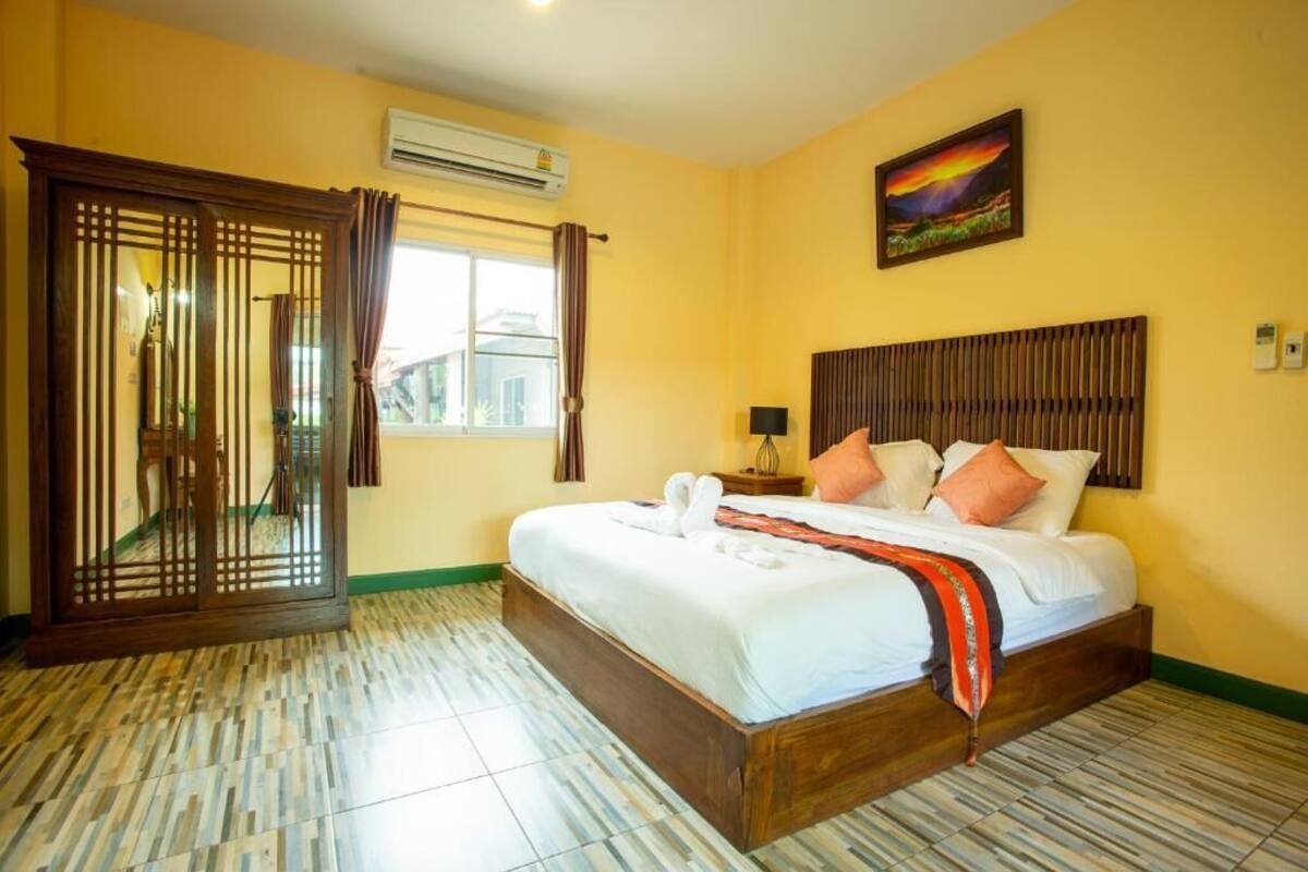 Ein Hotelzimmer mit Bett, Holz-Kopfstück, Fenster mit Vorhängen und einem Bild an der Wand.