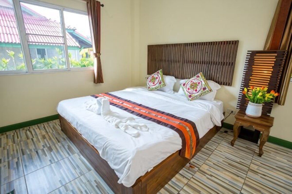 A hotel room with a bed, a bedside table with a plant, and a window with curtains.