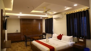 A hotel room with a bed, bedside table, chair, wardrobe, and a ceiling fan. - Hotel M Grand (Hyderabad)