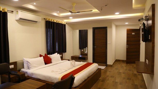 A hotel room with a bed, bedside tables, a desk, a chair, a ceiling fan, an air conditioning unit, and a television. - Hotel M Grand (Hyderabad)