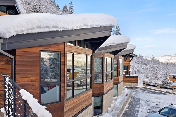 A modern wooden building with large windows and a sloped roof covered in snow.