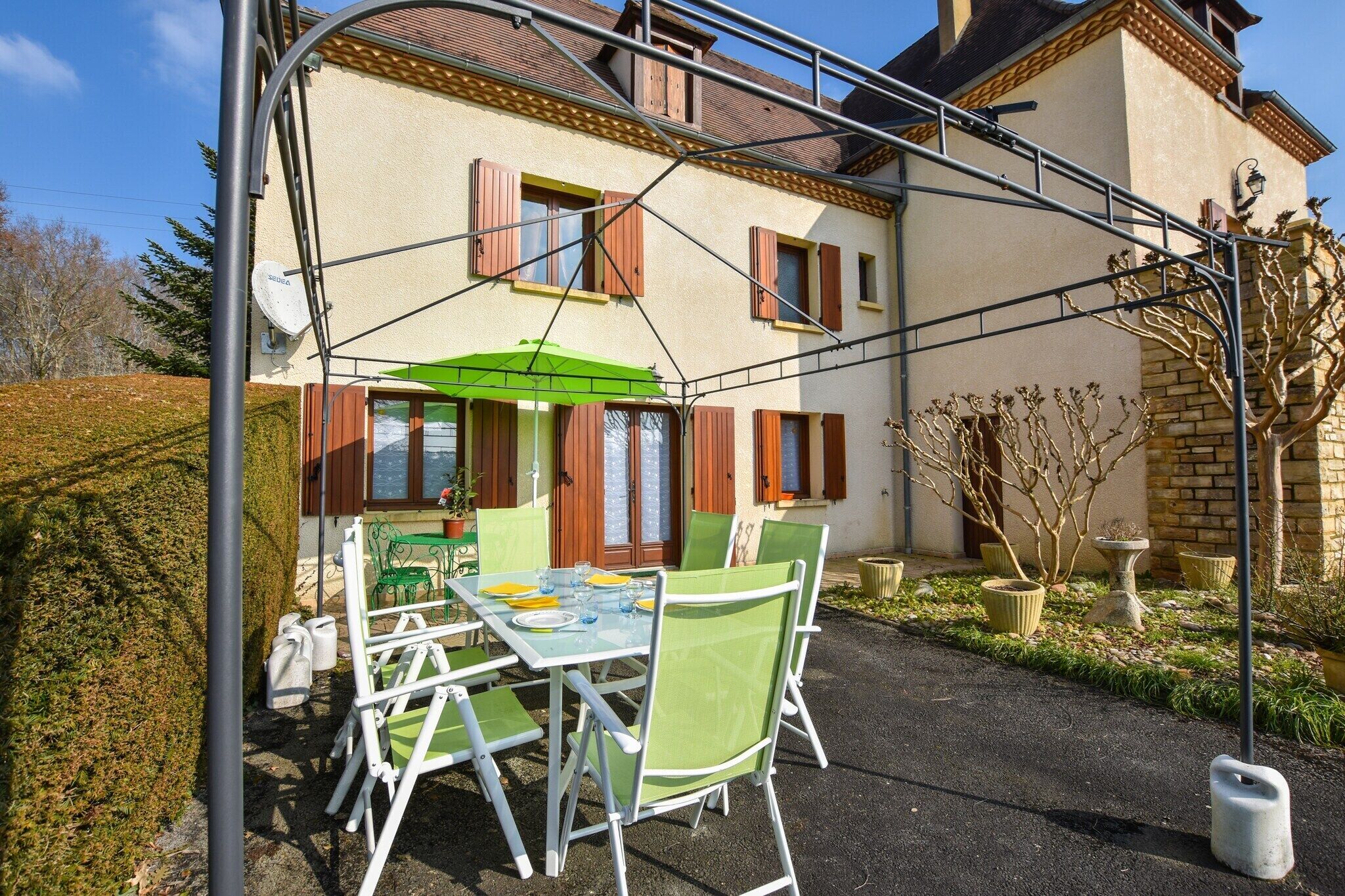 Een terras met een tafel, stoelen, een groene parasol en een gebouw met een bakstenen gevel en houten luiken.