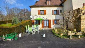 A two-story house with a patio area featuring a table and chairs, surrounded by a well-maintained garden and a stone wall. - House in Périgord near Medieval Villages (Prats du Périgord)
