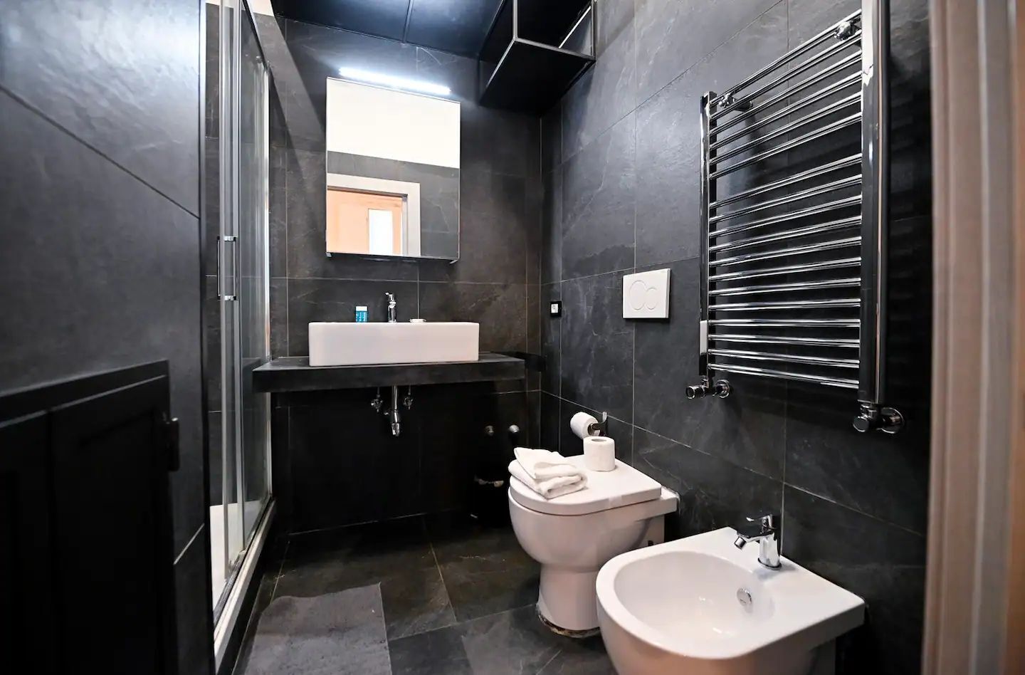 A modern bathroom with a large mirror, a white sink, a toilet, and a bidet.