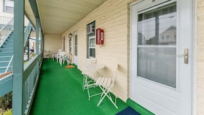 A covered porch with a green artificial turf floor, white folding chairs, a small table, and a door marked with the number 3.