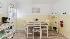 A compact kitchen with a dining table, chairs, a coffee maker, and a fire extinguisher.