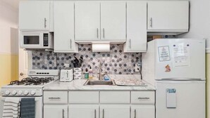 A kitchen with white cabinets, a microwave, a stove, a refrigerator, and a patterned backsplash.