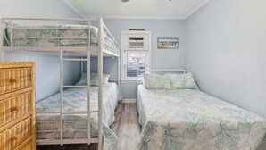 A bunk bed room with a ceiling fan, a window with blinds, and a wicker dresser.
