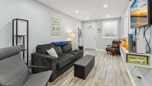 A modern living room with a grey sofa, a coffee table, a TV, and a wooden floor. - Modern 2 Bedroom Condo with Pool (Wildwood Crest)