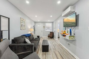 A living room with a sofa, a coffee table, a TV, and a wall-mounted shelf with toys. - Modern 2 Bedroom Condo with Pool (Wildwood Crest)