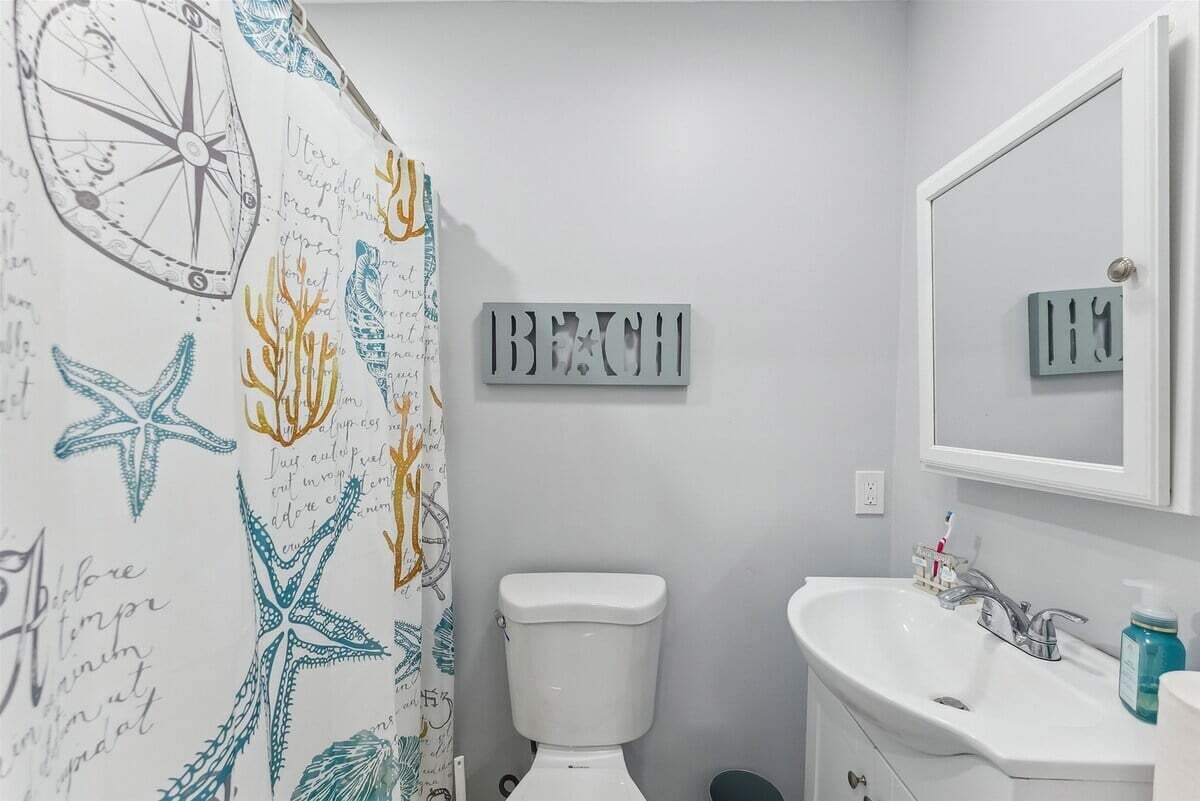 Un baño con cortina de ducha de temática náutica, inodoro, lavamanos y espejo.