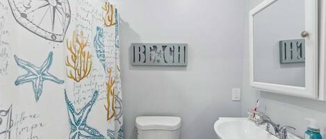 Un baño con cortina de ducha de temática náutica, inodoro, lavamanos y espejo.
